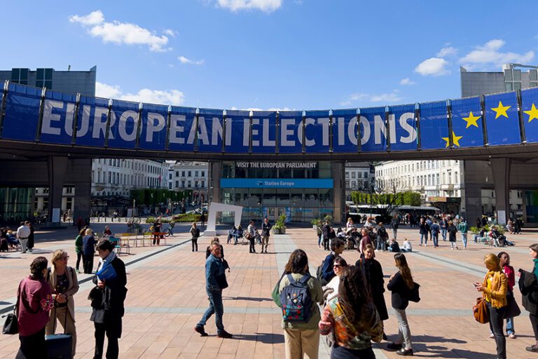 People,Walk,Toward,A,Banner,Advertising,The,European,Elections,Outside